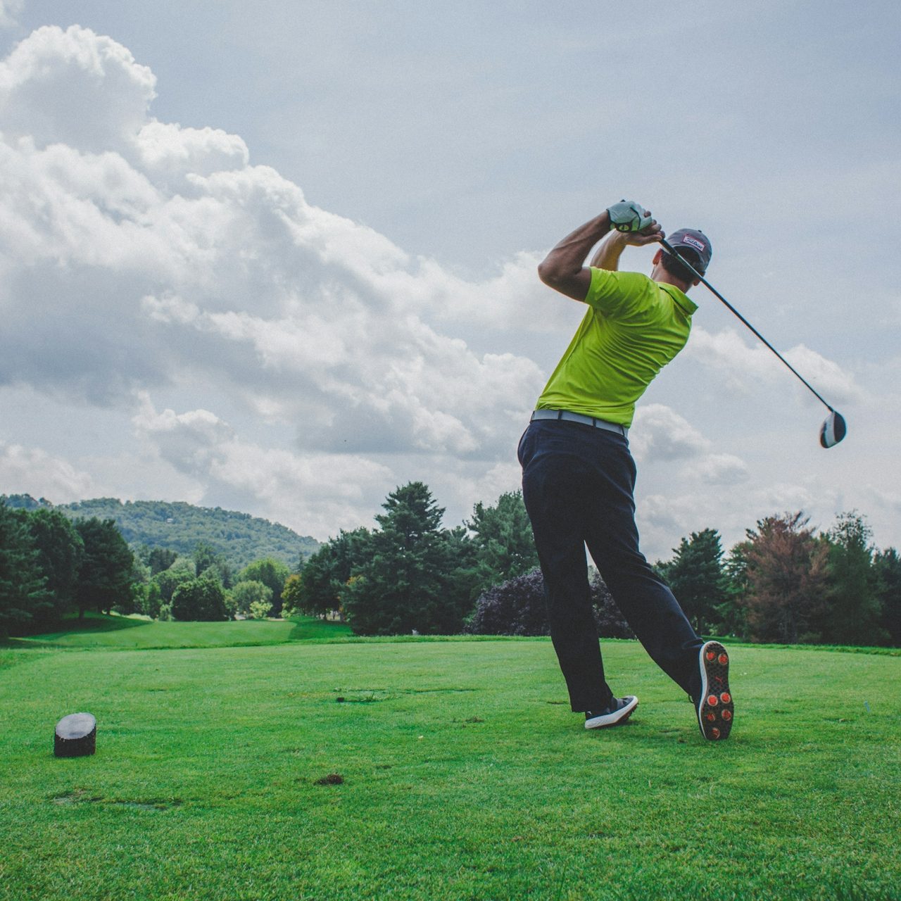 Golfspieler beim Abschlag auf einem grünen Platz unter bewölktem Himmel.