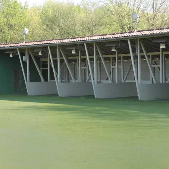 Driving Range mit mehreren überdachten Trainingsbereichen und grünem Belag.